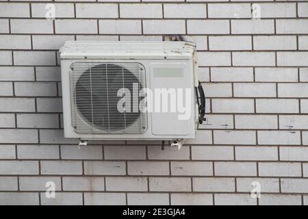 Air conditioning compressor unit on a white brick wall. Front view Stock Photo