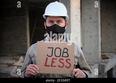 Engineer in mask and hardhat stands with placard Jobless Stock Photo