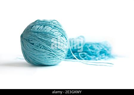 Theme of needlework. A ball of blue half-wound fine cotton yarn isolated on a white background. Tangled yarn in the background. Stock Photo