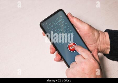 An elderly woman presses the SOS help button on the smartphone. Hands of an old man. Panic button, Technology. Stock Photo
