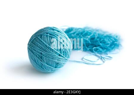 A ball of  blue fine cotton yarn in the process of winding, isolated on the white background. Tangled yarn in the background. Stock Photo