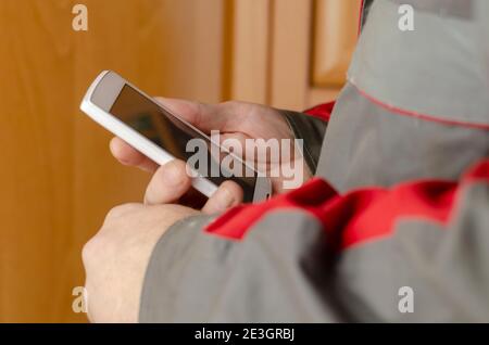 Close-up of a man's hands holding a white smartphone. Man wearing special clothes for work.  Special gray uniform with red inserts. Side view. Selecti Stock Photo