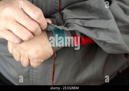 Special protective clothing for work. Man's hands are fastened with hook-and-loop clip on the sleeve of gray work jacket with red inserts. Close-up, s Stock Photo