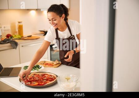 Contented lady making final steps in cooking pizza Stock Photo