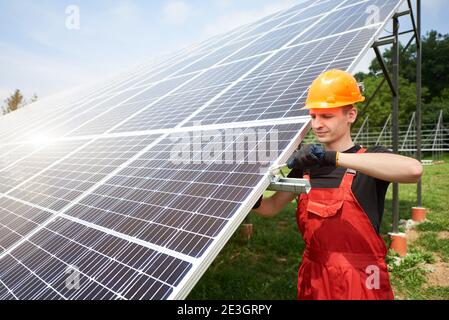Male technician checks the maintenance of the solar panels. Orange safety cap on his head. Concept: renewable energy, technology, electricity, service, green power. Stock Photo