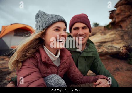 Happy young couple relaxing during camping sitting outside tent looking away during winter Stock Photo