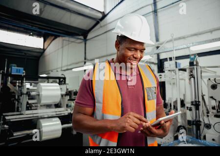 Happy male technician engineer checking process on digital tablet in large factory Stock Photo