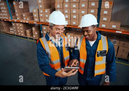 Young african man pointing something to his coworker over digital tablet in factory warehouse Stock Photo
