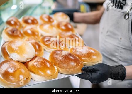 The baker has a tray of freshly baked butter buns and leaves them on a counter for sale at the bakery Stock Photo