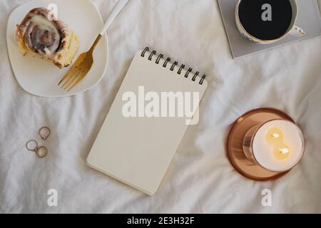 Notepad mock-up on the bed with cinnamon bun and burning candle. Stock Photo