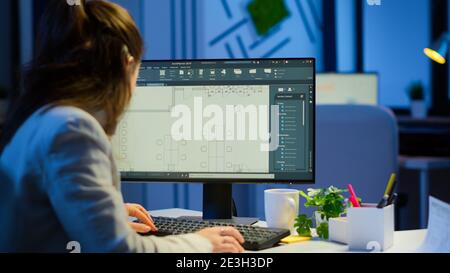 Over the shoulder shot of engineer working with architectural plans, cad software on desktop computer. Designer using arhitecture blueprints of buildings working overtime, creating and studying Stock Photo