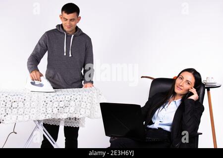 New modern standards. Business woman talks on the phone while sitting with a laptop while the man ironing things. White background. Stock Photo