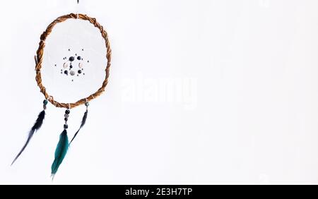 Banner with home decor in Scandinavian style. A unique mystical dream catcher made of willow vines, white threads, beads, and colored feathers. White Stock Photo