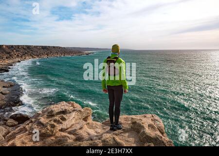 Trailrunner guy stands on the edge of a cliff by the sea on a sunny day. View from the back. Mangystau Peninsula. Kazakhstan Stock Photo
