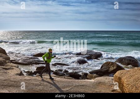 Treil running along the seashore. A man runs along the seashore among the stones on a sunny day. Off-road running Stock Photo