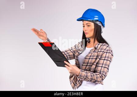 Serious female engineer in hard hat examines the plan and shows with his hand to the side on a white background. Stock Photo