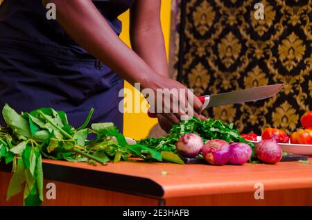 African chef carefully cutting vegetables with knife on the table Stock Photo