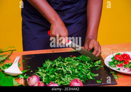 African chef carefully cutting vegetables with knife on the table Stock Photo