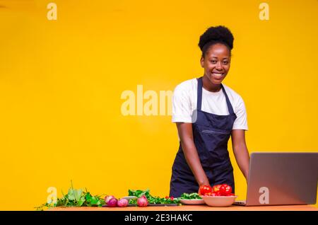 young beautiful african chef isolated over yellow background using her laptop to learn some cooking recipe online Stock Photo