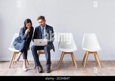 Smiling asian businesswoman sitting near businessman with laptop before job interview Stock Photo