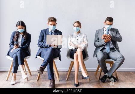 Multiethnic businesspeople in medical masks using devices before job interview Stock Photo