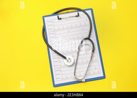 Stethoscope and clipboard with electrocardiogram on yellow background Stock Photo