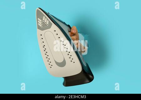 Female hand hold iron in hole on blue background Stock Photo