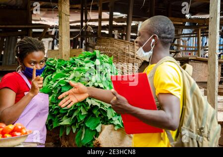 a young beautiful african market woman wearing face mask avoiding handshake from her customer Stock Photo