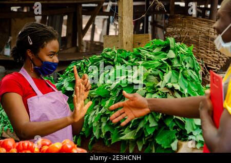 a young beautiful african market woman wearing face mask avoiding handshake from her customer Stock Photo
