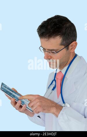 Caucasian doctor of medicine uses a tablet to view a chest x-ray, isolated on light blue background. Concept of technology in medicine Stock Photo