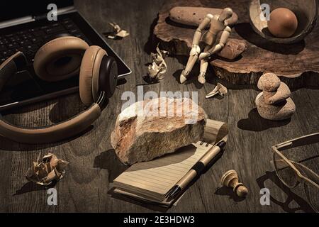 Writers Block. Concept still life, arrangement on dark wooden table. Heavy stone, brick on open blank block note. Laptop, earphones, glasses, stone Stock Photo