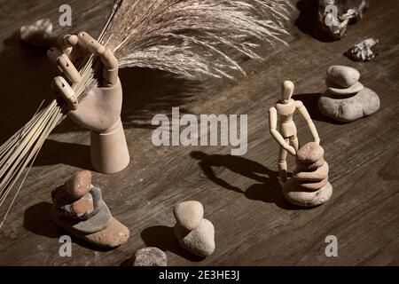 Wooden model hand holding dry withered pampas grass. Wooden human figure building zen stone pyramids. Finding inner balance in live. Surreal still Stock Photo