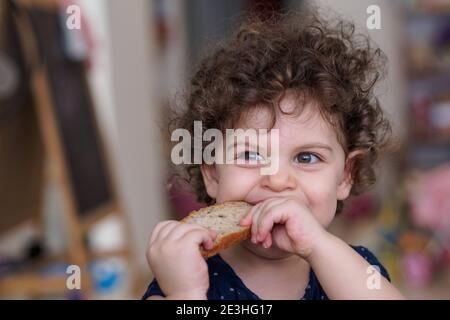 Young toddler siting at a table eating with her hands Stock Photo