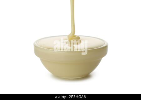 Condensed milk pouring in bowl, isolated on white background Stock Photo