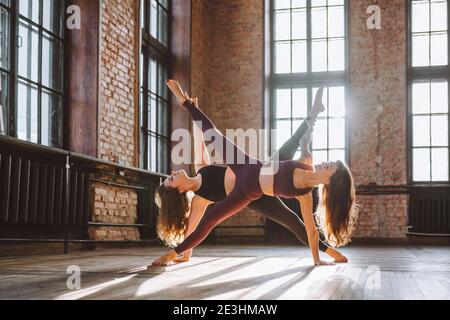 Star shape acrobatic composition made from two woman bodies in big loft room. Yoga, flexibility, healthy life. Stock Photo