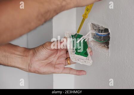 The electrician is using a screwdriver to check the power plug on the wall. Stock Photo