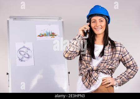 A woman architect is talking on the phone and smiling at the camera against the backdrop of an office project. Gender stereotypes. Stock Photo