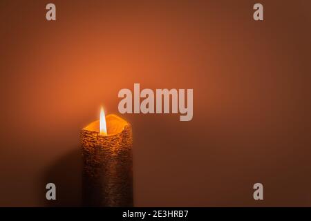 Orange patterned burning candle on dark orange background with copy space. Candlelight in dark orange environment. Single burning candle Stock Photo