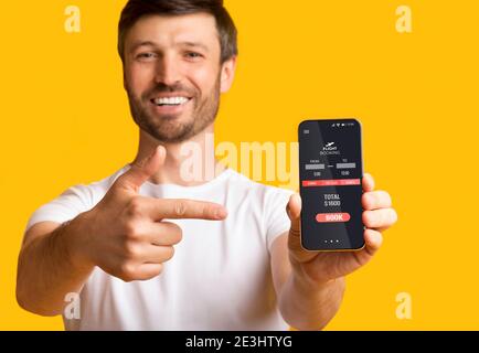 Man Pointing Finger At Smartphone Booking Flight Over Yellow Background Stock Photo