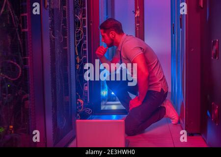Thinking man crouched near open servir rack Stock Photo