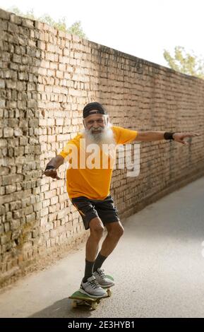 A BEARDED OLD MAN HAPPILY STANDING ON A SKATE BOARD Stock Photo