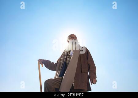 AN OLD MAN WITH WALKING STICK HAPPILY STANDING AND LOOKING AWAY Stock Photo