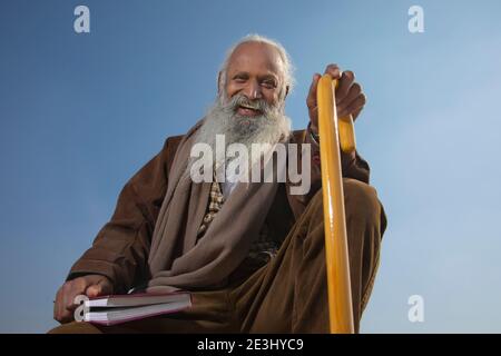 A BEARDED OLD MAN HAPPILY SITTING WITH BOOK IN ONE HAND Stock Photo