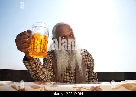 A BEARDED OLD MAN HAPPILY LOOKING AWAY WITH BEER IN HAND Stock Photo
