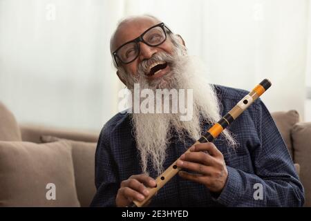 A BEARDED OLD MAN HAPPILY LAUGHING WHILE PLAYING FLUTE Stock Photo