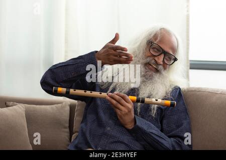 AN OLD MAN HAPPILY ENJOYING TIME BY PLAYING FLUTE Stock Photo