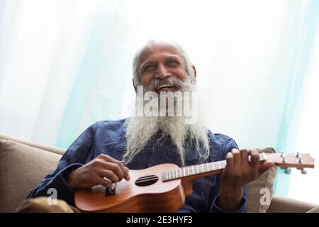 A HAPPY OLD MAN LOOKING ABOVE AND PLAYING UKULELE IN FREE TIME Stock Photo