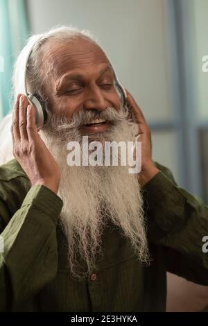 A BEARDED OLD MAN HAPPILY LISTENING TO MUSIC ON HEADPHONES Stock Photo