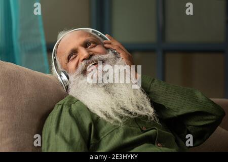 A HAPPY OLD MAN SITTING COMFORTABLY AND LISTENING TO MUSIC Stock Photo