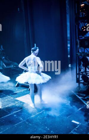 Ballet dancer in the wings in white tutu wating to go on stage during a performance of Swan Lake, surrounded by blue lighting and dry ice Stock Photo